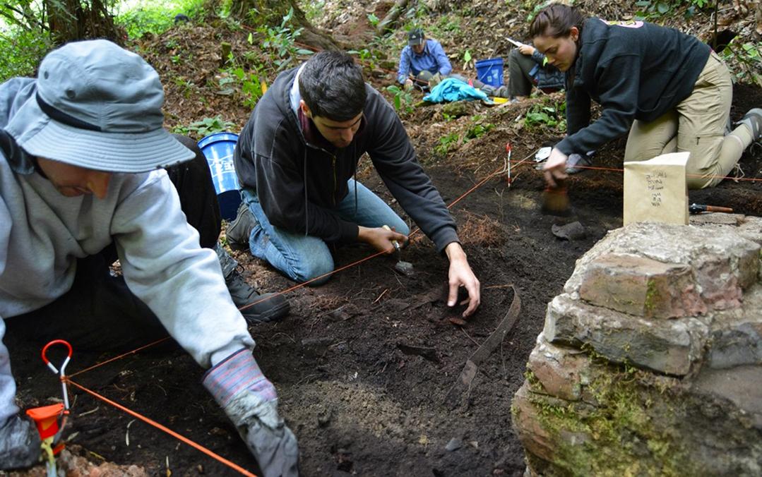 Anthropology students crouch down on the dirt as they dig up a targeted area on the ground.